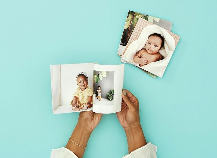 hands opening photo book with baby on pages and stack of softcover photo books nearby