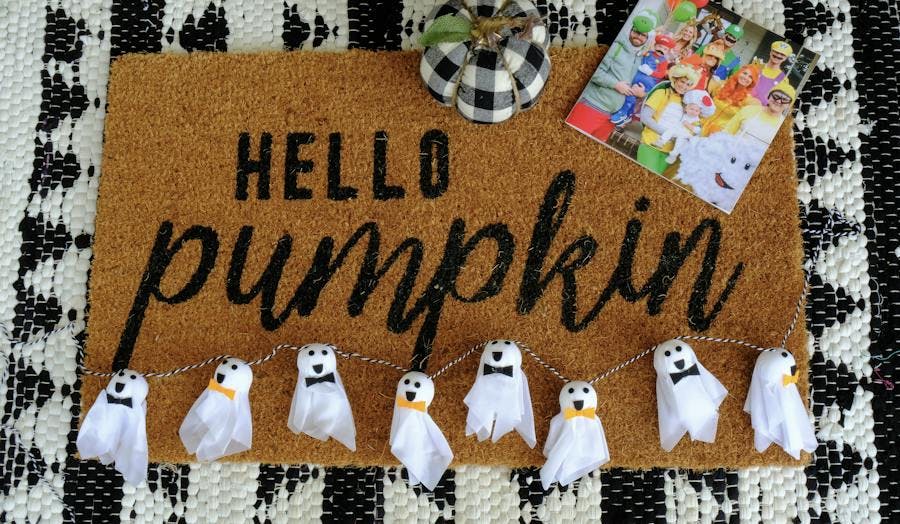 A hello pumpkin doormat with a homemade Halloween garland, pumpkin, and Chatbook on the mat. 