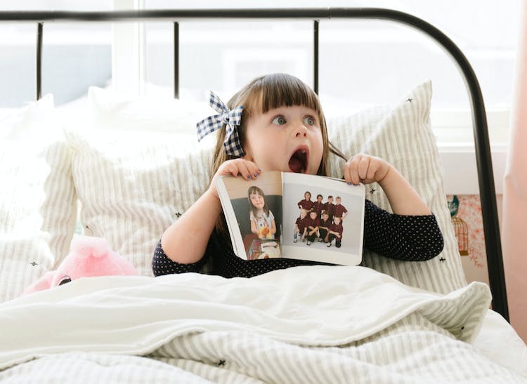 little girl sitting in bed looking surprised while holding monthly photo book