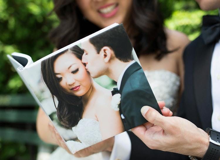 hand holding wedding photo album with groom kissing bride on hardcover